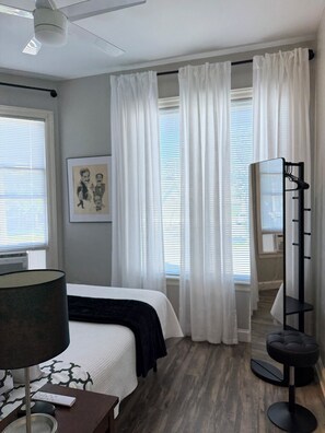 A hotel room with a bed, a standing mirror, a lamp, and a framed picture on the wall.