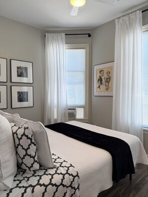 A bedroom with a bed, a bedside table, a chair, and a window with curtains. - Hip Suite-1st Floor - Arts District/Farmers Mkt/Cafes/Breweries-Near Lake George (Glens Falls)