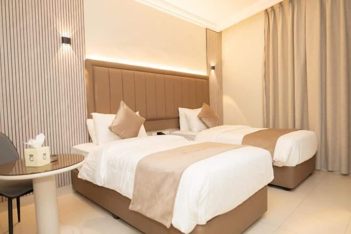 A hotel room with two beds, a small table, and a bedside table with a lamp.
