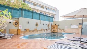 A swimming pool with lounge chairs and umbrellas, surrounded by a tiled patio and a building with a blue awning. - Captain's Hotel (Aqaba)