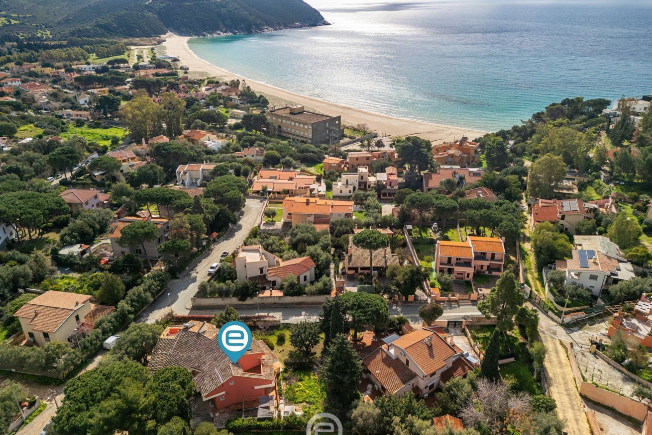 An aerial view of a coastal town with a beach, houses, and greenery.