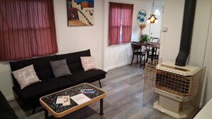 Un salon avec un canapé noir, une table basse sur laquelle se trouvent des papiers, un tableau accroché au mur et une cheminée.