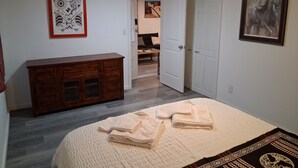 Une chambre à coucher avec un lit, une commode en bois, une porte blanche et un tableau accroché au mur.