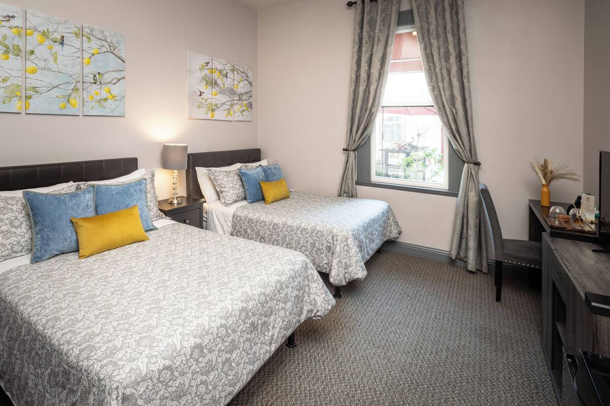 A hotel room with two beds, a desk, a chair, a lamp, and artwork on the walls.