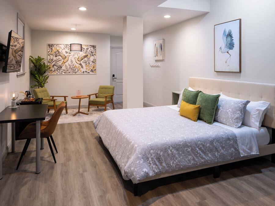 A modern hotel room with a large bed, a dining table, two chairs, a small table, and artwork on the walls.