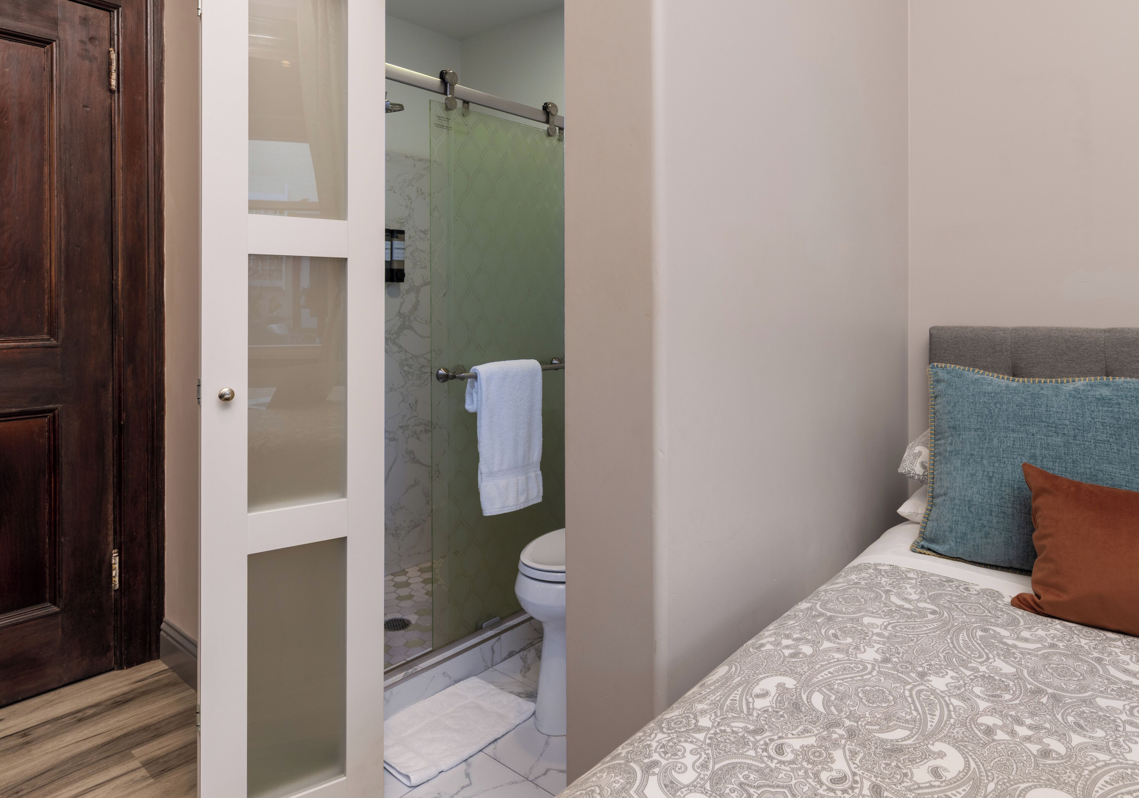 Un baño con cabina de ducha de vidrio, inodoro y toalla blanca colgada en la pared.