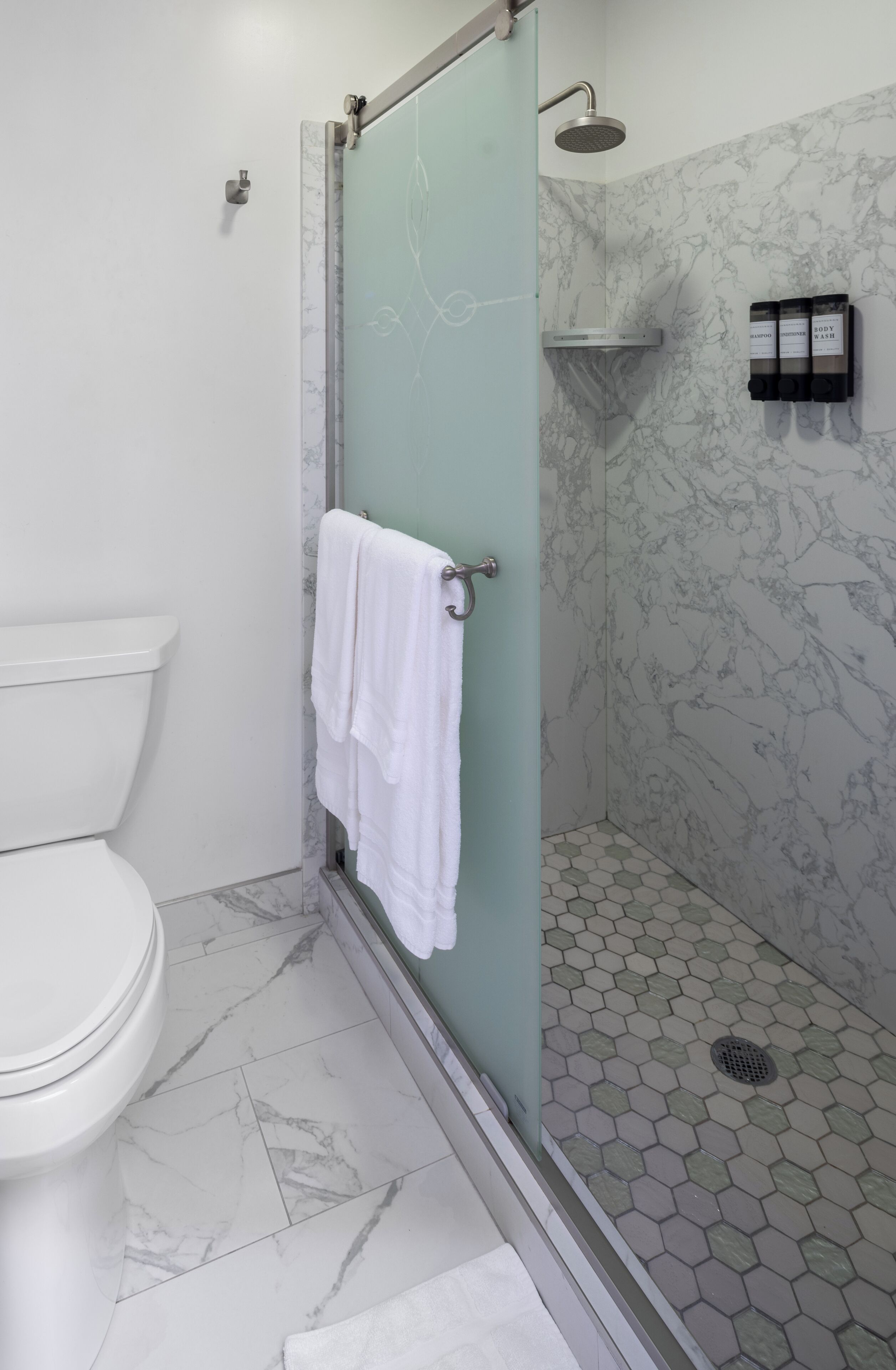 A bathroom with a toilet, a glass-enclosed shower with a handheld showerhead, and a towel rack with a white towel.