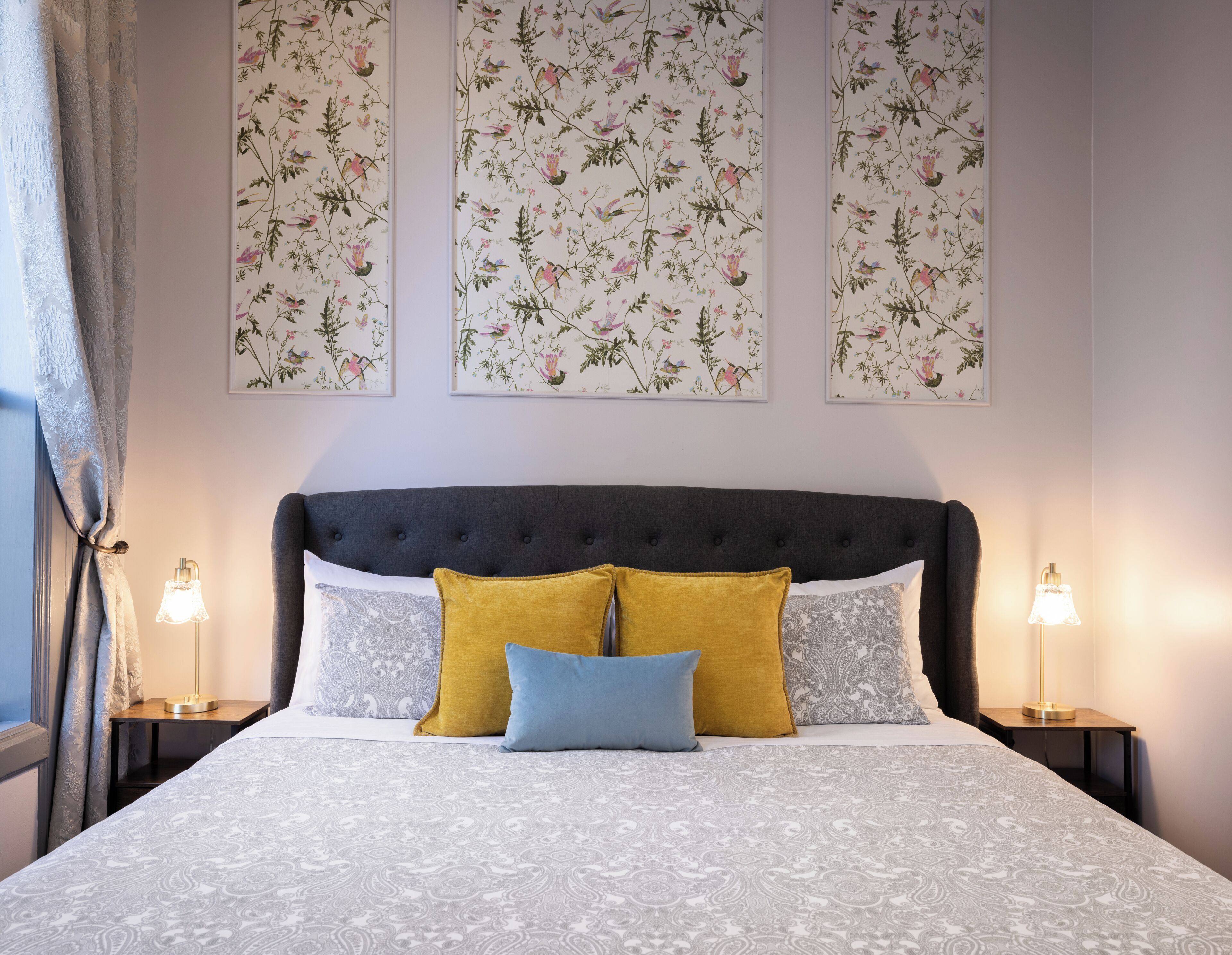 Un dormitori amb un capçal tapissat, roba de llit estampada i decoració floral a les parets.