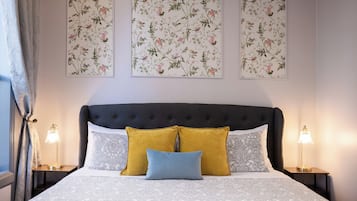 A bedroom with a tufted headboard, patterned bedding, and floral wall art.