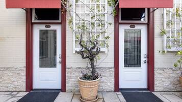Un edificio con dos puertas blancas, cada una con un toldo rojo, y una planta en maceta al frente.
