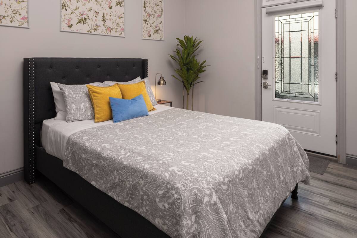 A bedroom with a bed, a nightstand, a potted plant, and a door with a window.