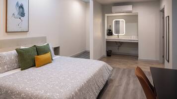 A bedroom with a bed, a bedside table, a chair, a bathroom with a mirror, and an air conditioner.