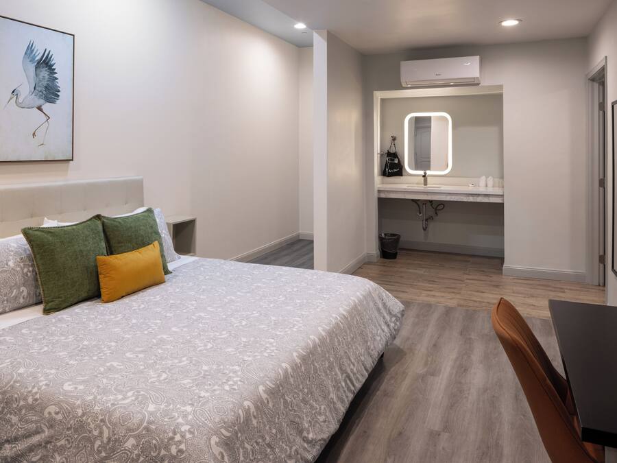 A bedroom with a bed, a bedside table, a chair, a bathroom with a mirror, and an air conditioner.