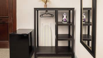 A black console table with a hanging garment, a small shelf with an iron, and a vase with dried plants.