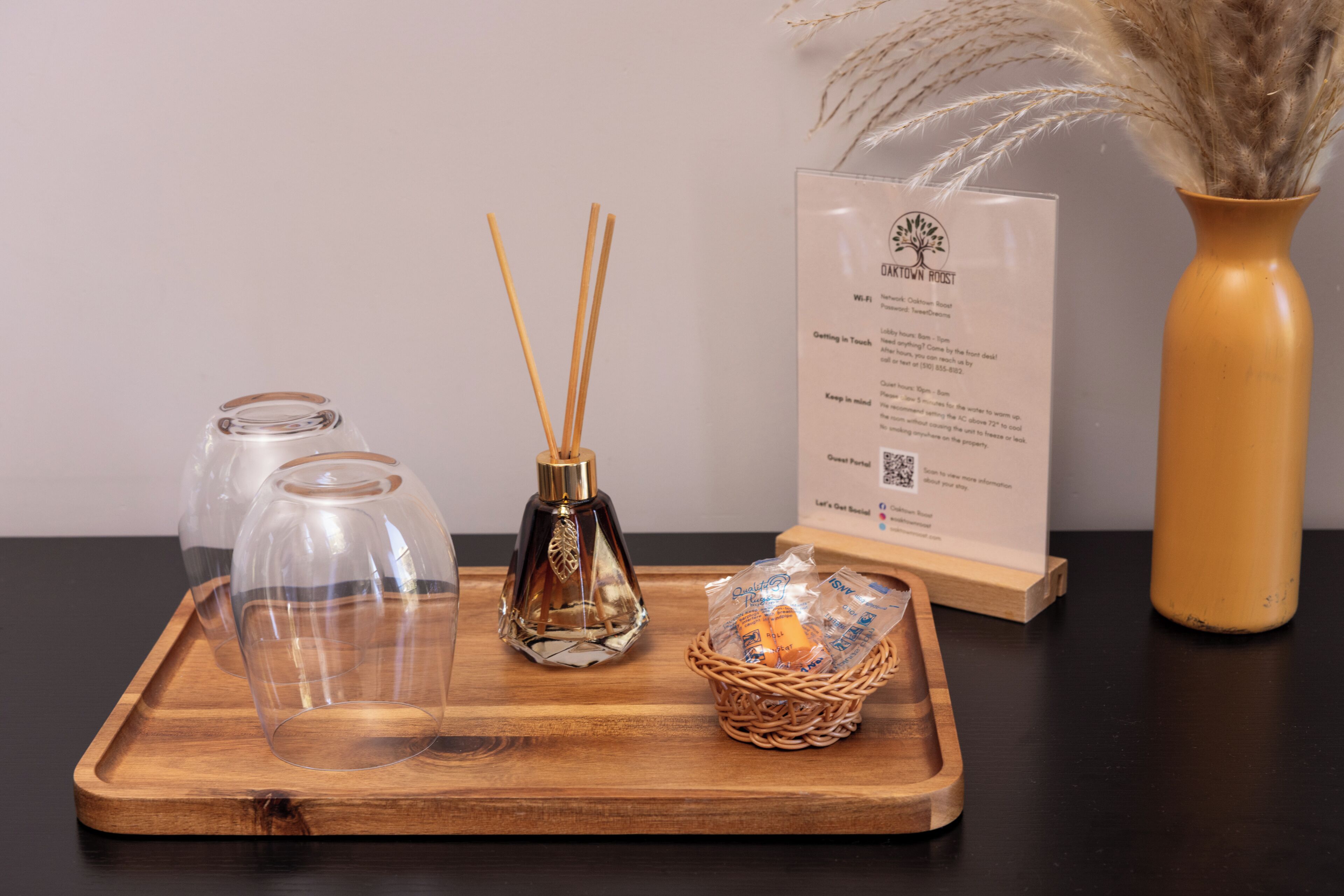 A wooden tray with two glass bottles, a reed diffuser, and a wicker basket with candles.
