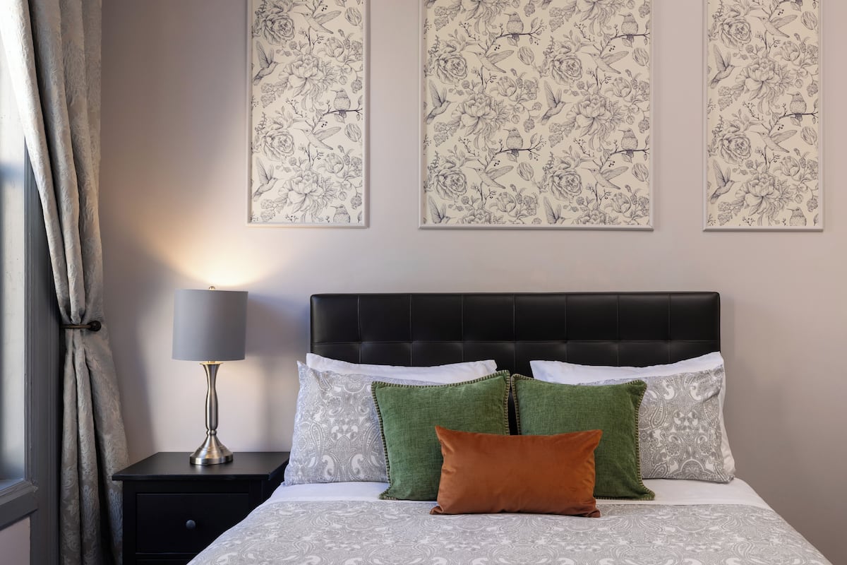 A bedroom with a bed, nightstand, lamp, and floral wall art.