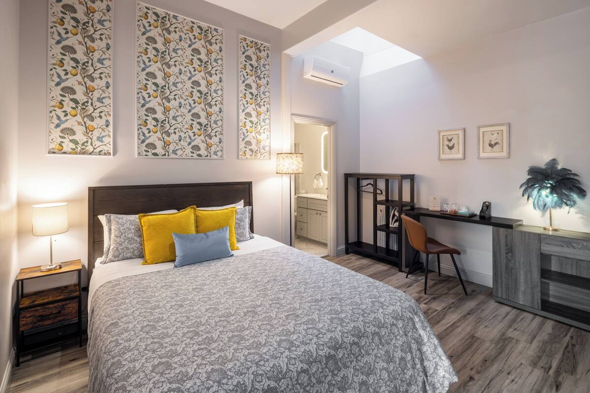 A bedroom with a bed, bedside table, lamp, and a desk with a chair.