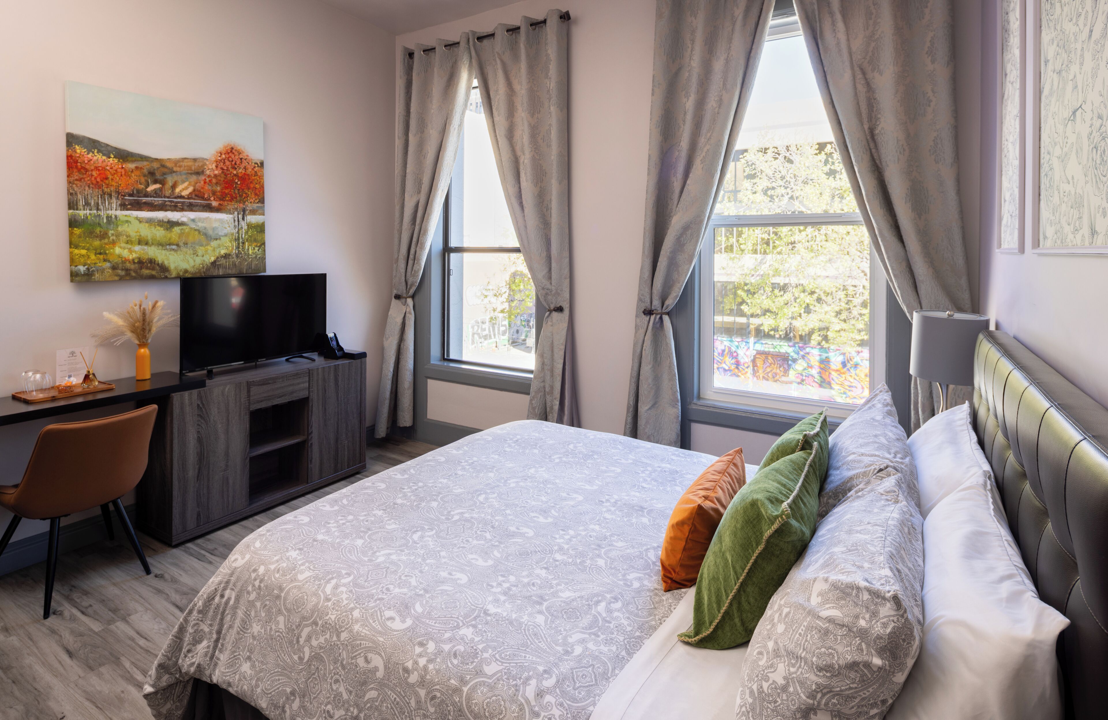 A bedroom with a bed, a desk, a TV, and a window with curtains.
