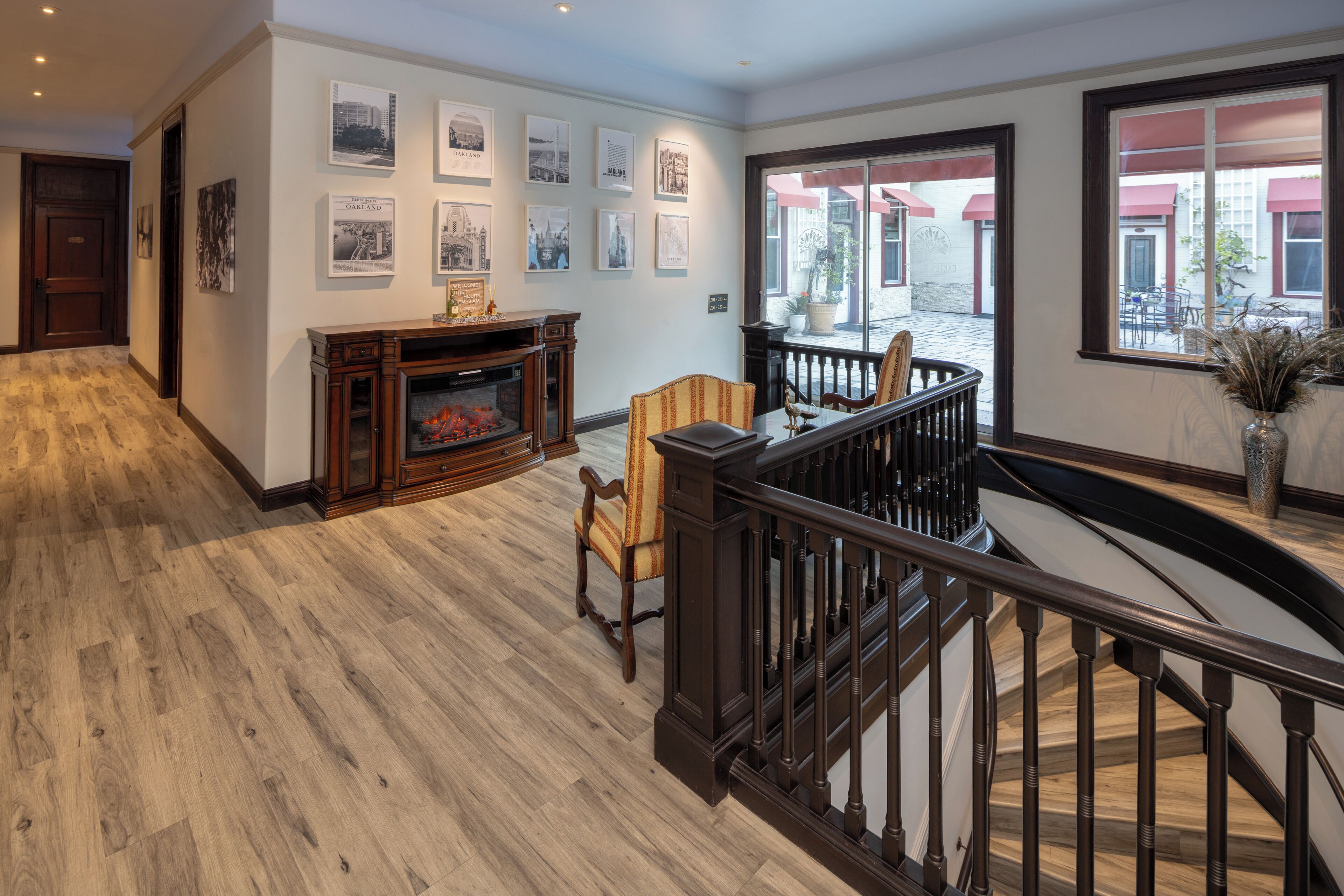 A spacious interior with a wooden floor, a fireplace, a staircase, and artwork on the walls.