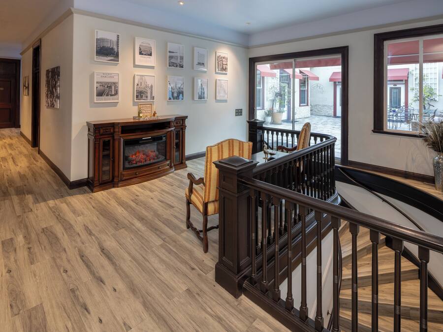 A spacious interior with a wooden floor, a fireplace, a staircase, and artwork on the walls.