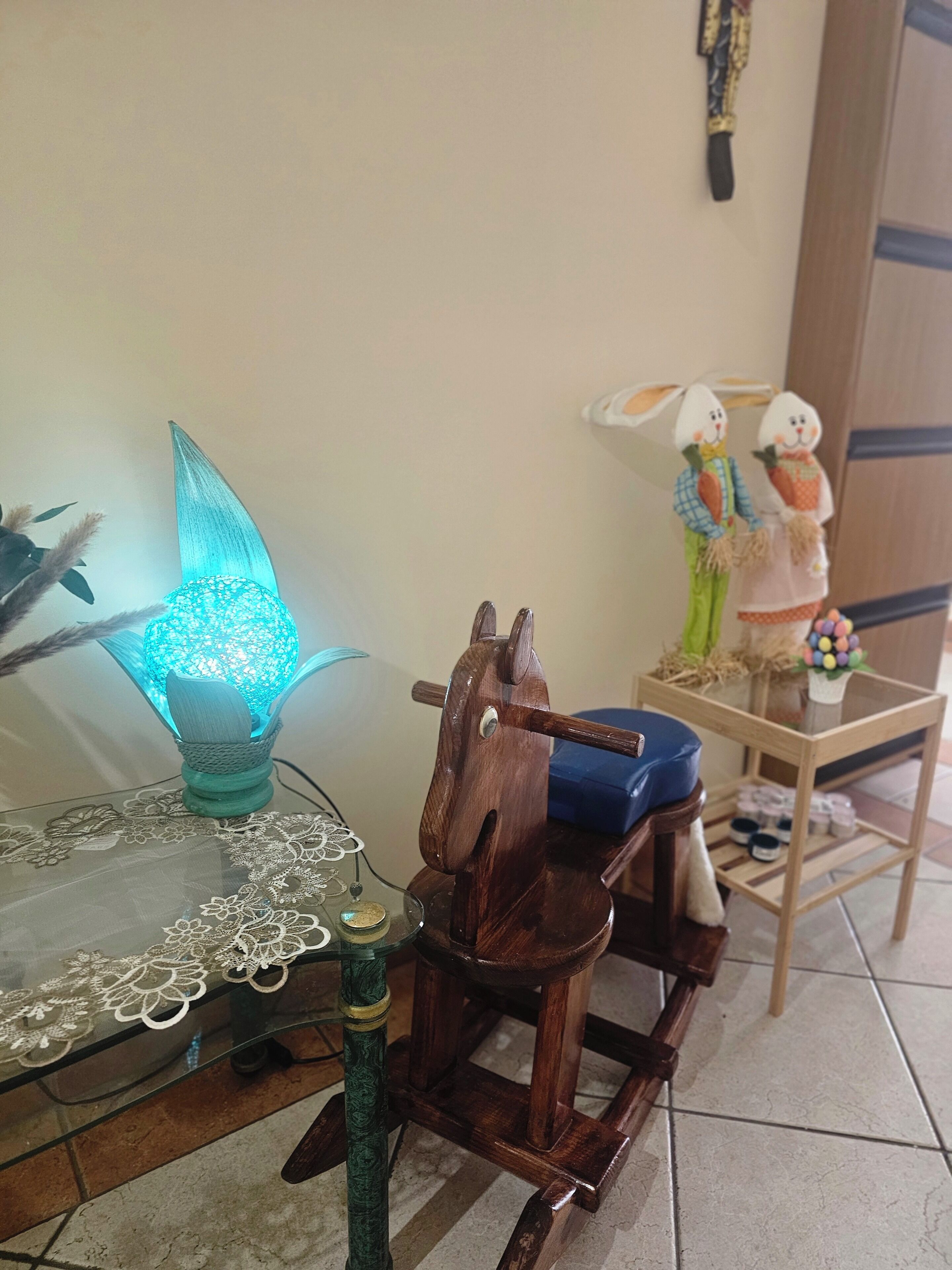 Een houten schommelpaard, een blauwe lamp en een klein tafeltje met een kantkleed.