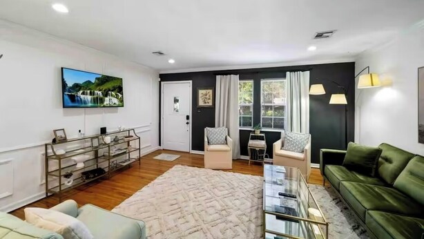 A modern living room with a green sofa, a glass coffee table, and a TV mounted on the wall. - Near Gathering Pl, River Park Trails, Brookside shops (Tulsa)