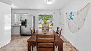 A dining area with a wooden table and chairs, a kitchen with a refrigerator and a window, and a hammock with starfish decorations on the wall. - Villa Pausa - 3 bedroom house in Gurabo (Gurabo)