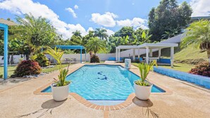 A swimming pool with a tiled deck, surrounded by potted plants and a covered seating area. - Villa Pausa - 3 bedroom house in Gurabo (Gurabo)