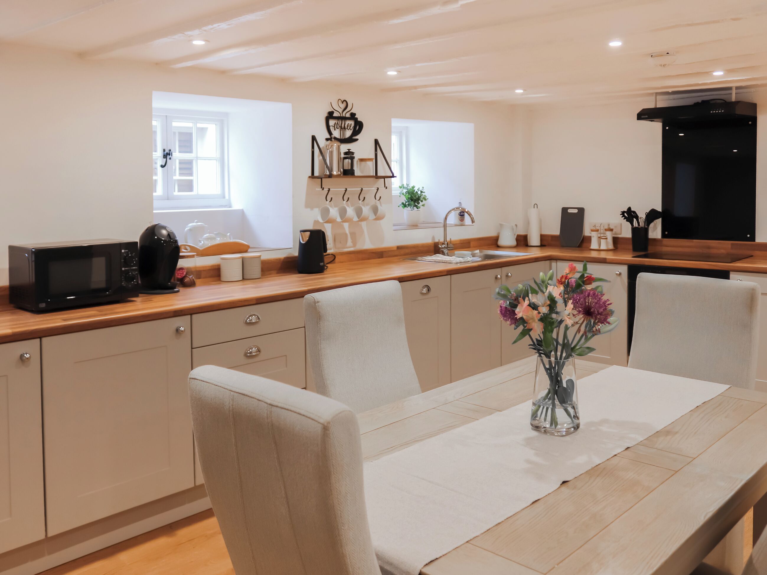 Una cocina moderna con encimera de madera, una mesa de comedor con sillas, una cafetera y un florero con flores.