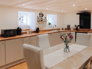 A modern kitchen with a wooden countertop, a dining table with chairs, a coffee machine, and a vase with flowers. - 2 bedroom accommodation in Conwy (Conwy)