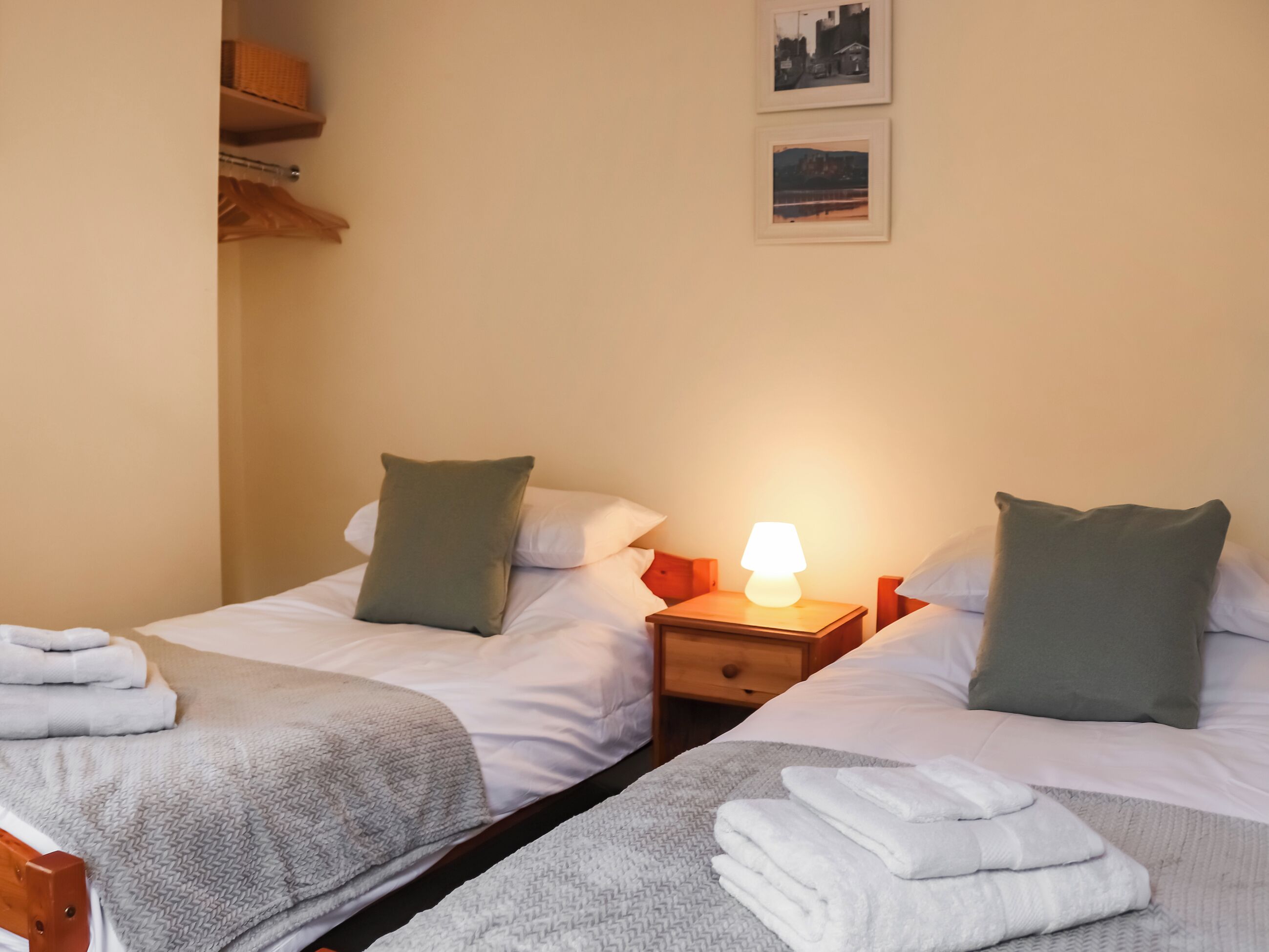 A twin room with two beds, each with a pillow, a nightstand with a lamp, and a small drawer.