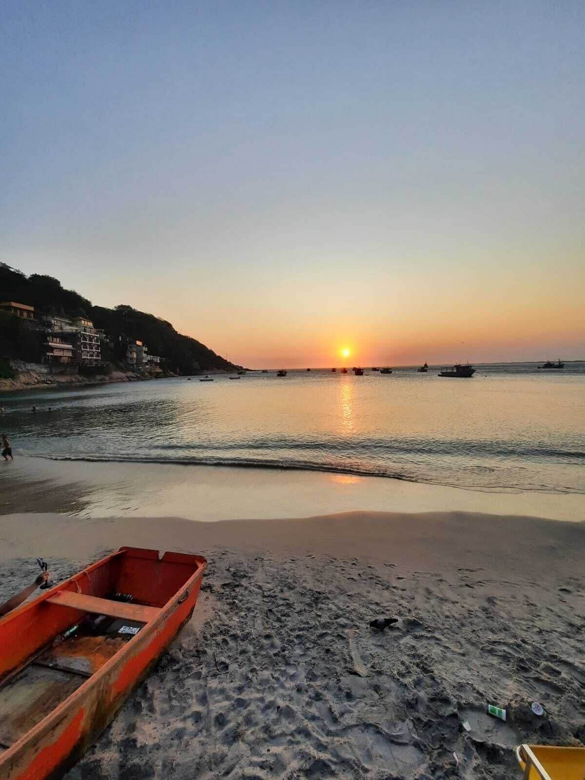 A beach with a sunset, calm water, and a row of buildings on the left.