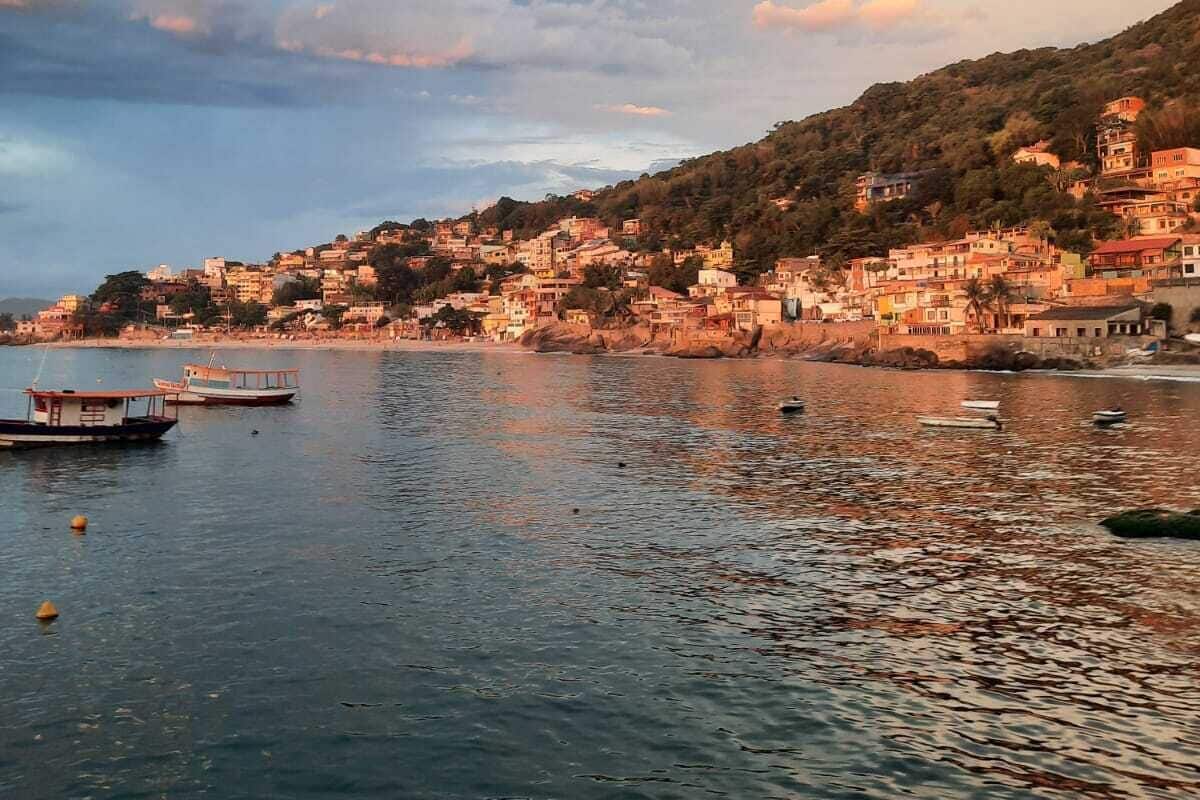 Μια παραθαλάσσια πόλη με κτίρια χτισμένα σε μια πλαγιά, βάρκες στο νερό και έναν καθαρό ουρανό.