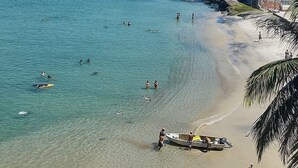 A coastal beach with clear waters, a sandy shore, and buildings in the background. - Pousada ilha Bella  (Rio de Janeiro)