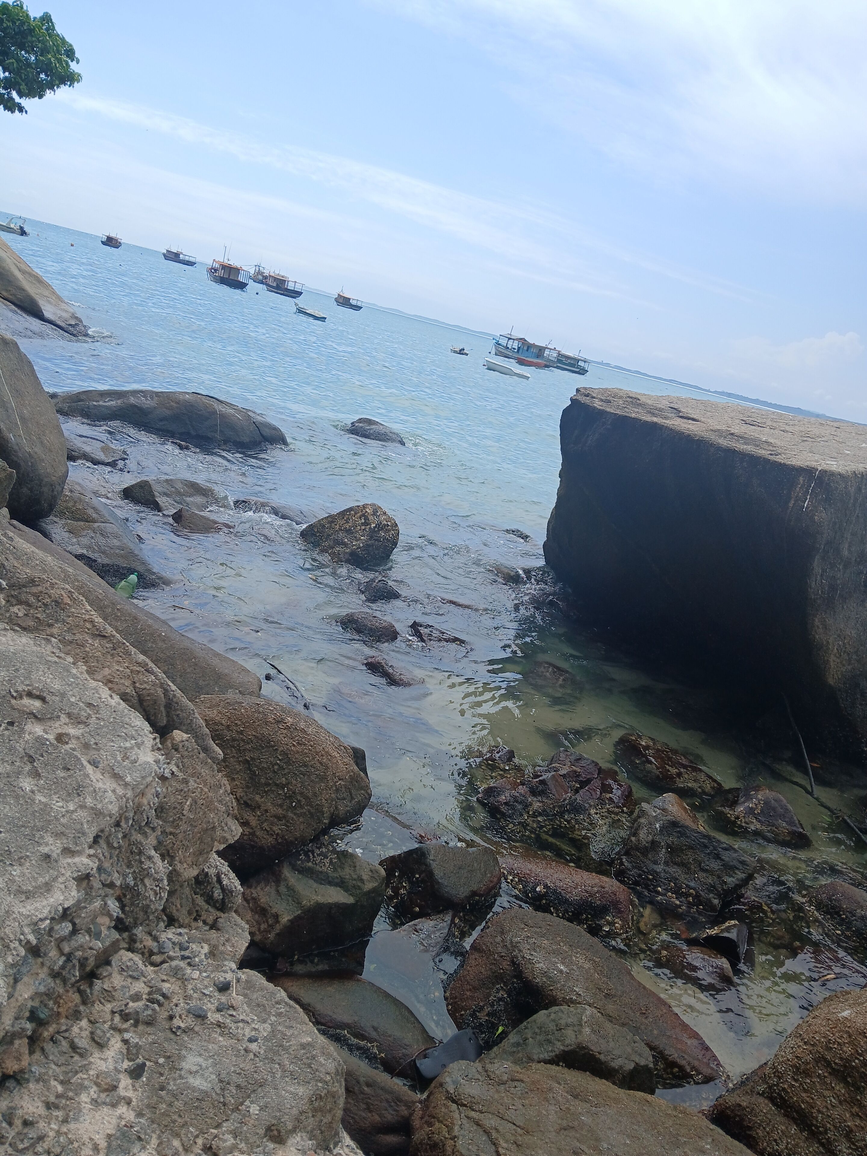 Una costa rocosa con aguas cristalinas y barcos a lo lejos.