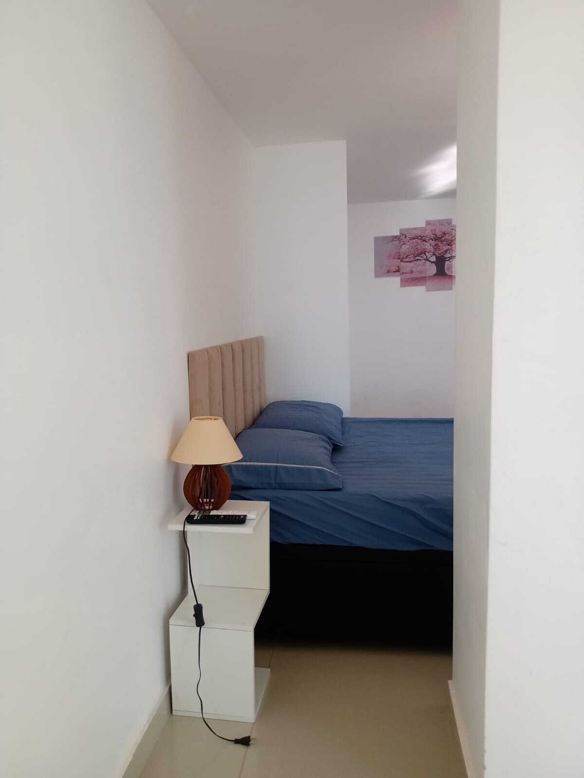 A bedroom with a bed, a nightstand with a lamp, and a wall-mounted picture.