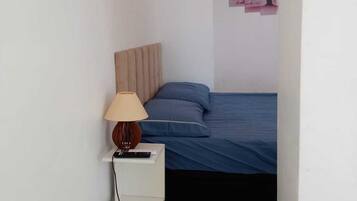A bedroom with a bed, a nightstand with a lamp, and a wall-mounted picture.
