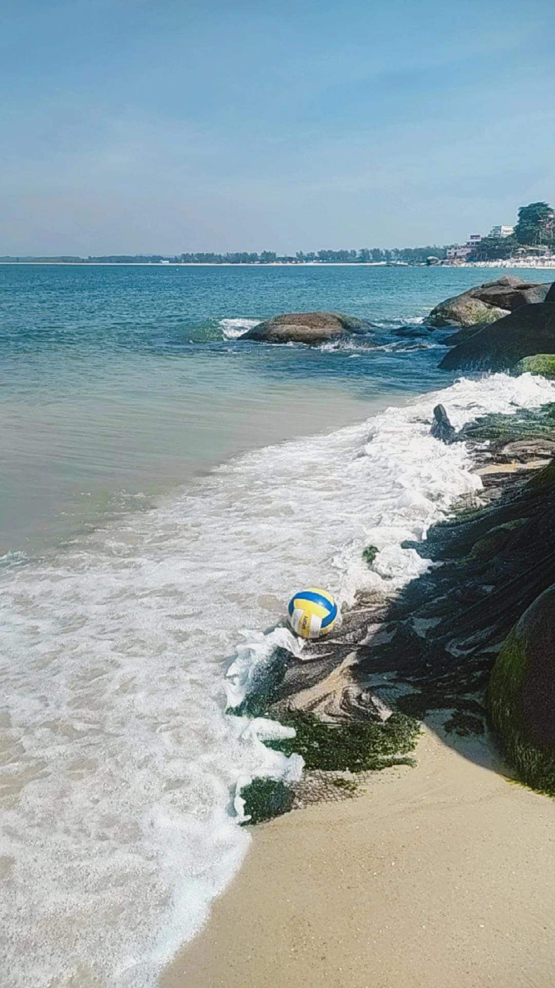Uma praia com ondas, uma bola de vôlei e pedras.