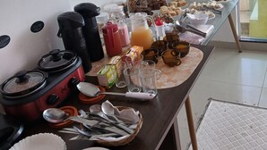 A breakfast buffet with various food items and beverages, a stove, and kitchen utensils. - Pousada ilha Bella  (Rio de Janeiro)
