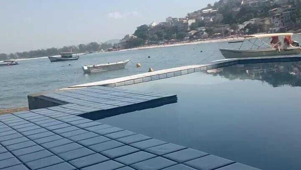 A pool area with tiled flooring and a view of boats on the water. - Pousada ilha Bella  (Rio de Janeiro)