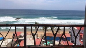 A view of the ocean from a covered balcony with a metal railing, overlooking a beach with buildings in the background. - New ad (Zipolite)