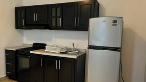 A compact kitchen with black cabinets, a stainless steel refrigerator, a stove, and a sink. - Grecas del mar house. (Zipolite)