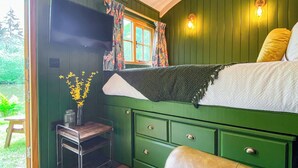 A green room with a bed, a small table with a vase of flowers, and a window with curtains.