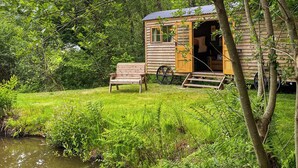 A wooden cabin with a porch, a bench, and a wheelbarrow.