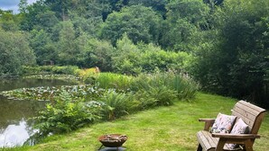 A wooden bench with floral cushions by a pond surrounded by lush greenery.