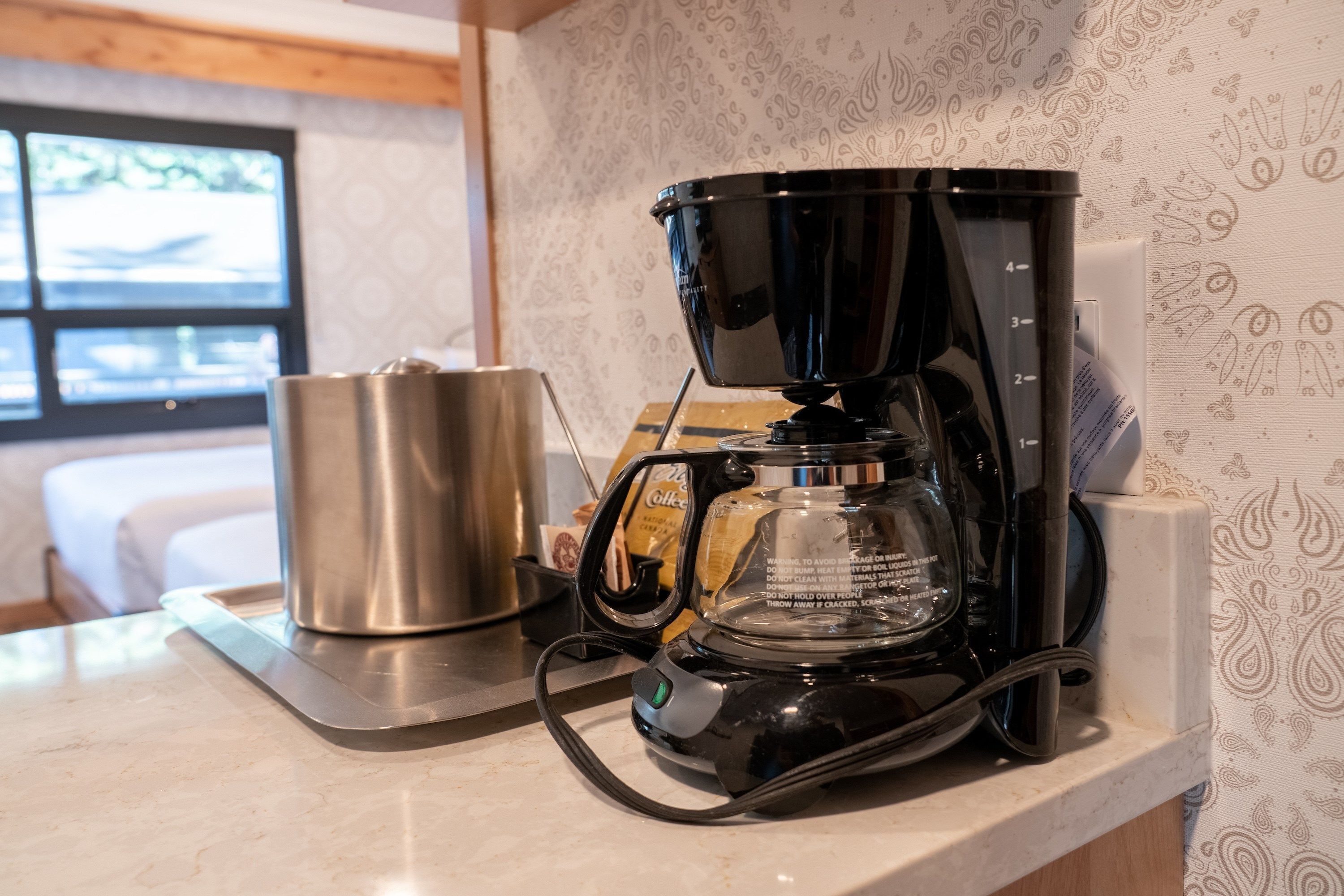 A coffee maker on a kitchen counter with a stainless steel pot and a glass carafe.
