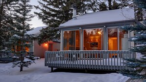 A snow-covered cabin with a glass front, a wooden deck, and a chimney.