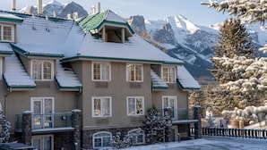 A multi-story building with a snow-covered roof and a view of snow-capped mountains in the background. - Mountain Getaway with Free Breakfast (Canmore)