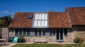A stone building with a tiled roof, multiple windows, and a bench in front.