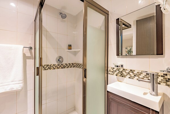 A bathroom with a glass shower door, a white sink, a mirror, and a tiled backsplash.